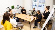 7 Personen im Austausch miteinander um einen Tisch herum