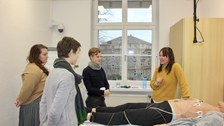 3 Teilnehmende und Dozierende stehen um Dummy mit Elektroden in der Station sensorbasiertes Feedback zur Positionierung von EKG Elektroden
