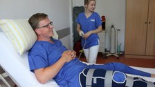 Eine Person liegt im Bett und eine weitere Person steht daneben