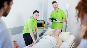 Simulationsperson im Krankenbett und um ihn herum studentische Tutoren und Studierende während einer Lehreinheit