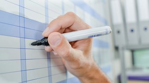 Das Foto zeigt die Hand einer Person, die gerade mit einem schwarzen Marker etwas in einen Kalender schreibt.