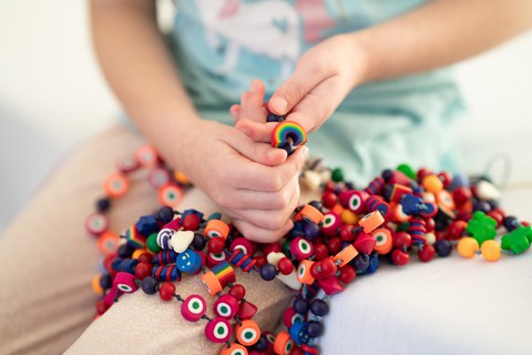 Nahaufnahme von Kinderhänden, die zusammengebundene Mutperlen halten.