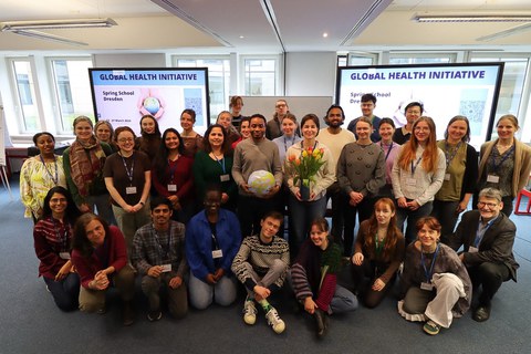 Rund 30 Menschen posieren vor der Kamera. Im Hintergrund zwei Bildschirme mit dem Text "Global Health Initiative"
