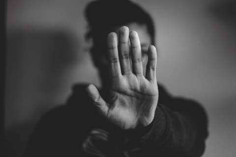 Eine Person hält abweisend die Hand vor ihr Gesicht. Man blickt auf die Handfläche.