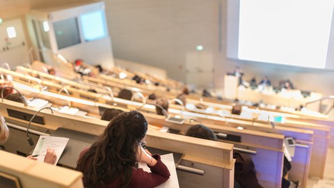 Ein volles Hörsaal; Menschen folgen einem Vortrag und machen Notizen