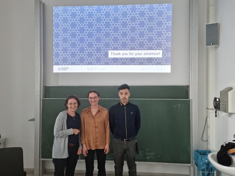 Zwei Frauen und ein Mann stehen vor einer Tafel über der eine Präsentationsfolie gezeigt ist auf der Thank you for your attention steht.