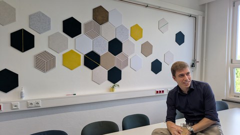 Mann mit Getränk vor einer Wand geschmückt mit sechseckigen Paneelen