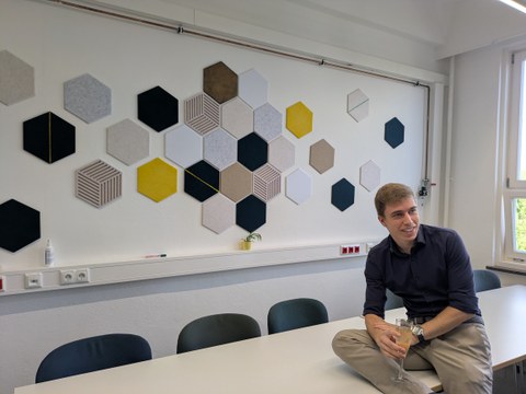 Mann mit Getränk vor einer Wand geschmückt mit sechseckigen Paneelen