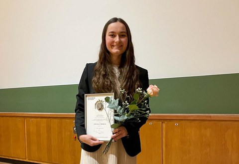 Brünette Frau mit rosa Rose und Auszeichnung in der Hand.