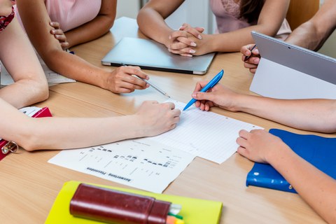 Foto: Blick von oben auf einen Arbeitstisch. Hände zeigen auf ein Blatt mit Diagrammen.