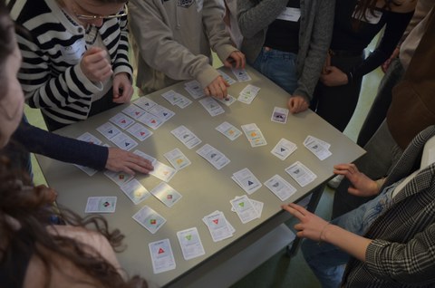 Elementarteilchen-Steckbriefe in Spielkartenform werden auf einem Tisch sortiert