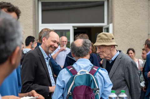 Drei Männer stehen auf einer Terrasse und sind im Gespräch. 