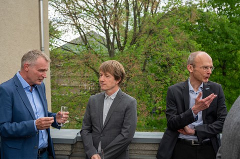 Drei Männer stehen auf einer Terrasse und sind im Gespräch.
