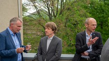 Drei Männer stehen auf einer Terrasse und sind im Gespräch.