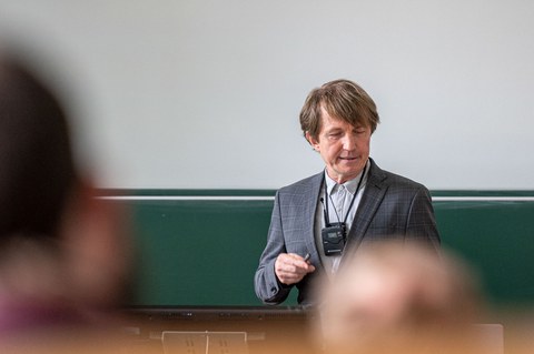 Ein Mann steht in einem Hörsaal mit dem Rücken zur Tafel.