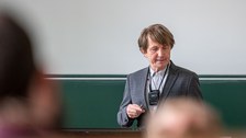 Ein Mann steht in einem Hörsaal mit dem Rücken zur Tafel.