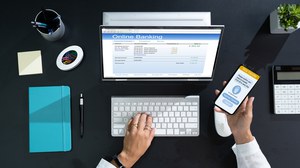Bild zeigt eine Person, die an ihrem Schreibtisch am Laptop sitzt und sich per 2-Faktor Anmeldung beim Online Banking anmeldet