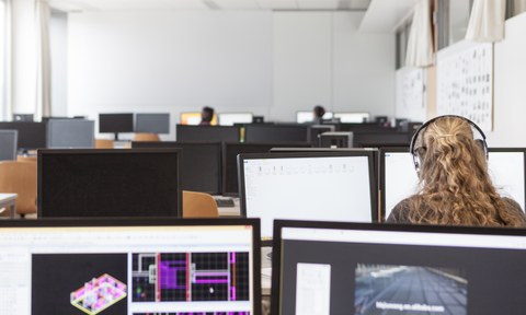 Eine Person mit Kopfhörern sitzt an einem PC in einem PC-Pool.