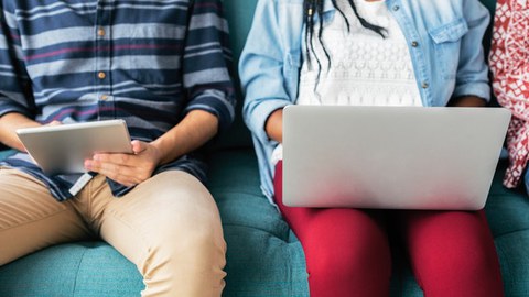 Sitzende Personen mit Tablet und Latop auf dem Schoß