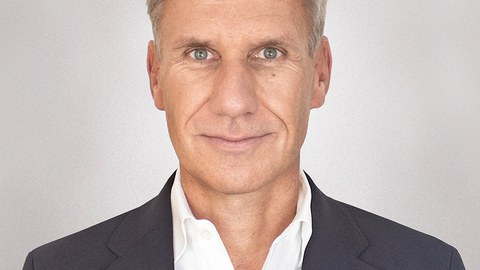 Portraitaufnahme von Prof. Markus Scholz, ein weißer Mann mittleren Alters, der einen Dunklen Anzug trägt