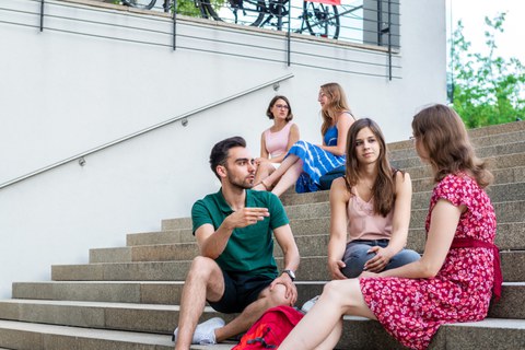 Fünf Studenten sitzen in lockerer Atmosphäre auf einer Treppe und unterhalten sich.