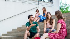 Fünf Studenten sitzen in lockerer Atmosphäre auf einer Treppe und unterhalten sich.