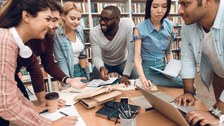 Foto von sechs Studenten aus verschiedenen Ländern, die zusammen in der Bibliothek fröhlich lernen.