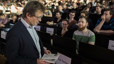 Ben Feringa mit einem Buch vor den gefüllten Reihen des Audimax