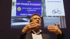 Ben Feringa bei seinem Vortrag vor einem seiner Slides, das eine Auto- und eine Fahrrad-Park-Plakette für Nobelpreisträger zeigt