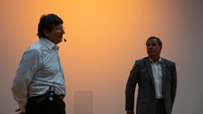 Andre Geim und Clemens Kirschbaum vor einer orange beleuchteten Wand.