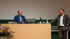 Redner am Pult und Mann mit Mikrofon lachen