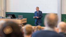 Ein Mann steht vor der Tagel und spricht ins Mikrofon.