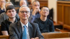 Hinter einem Mann sitzen viele Menschen im Hörsaal