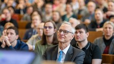 Hinter einem Mann sitzen viele Menschen im Hörsaal