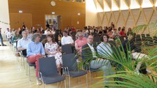 In einem großen Saal sitzen viele Menschen. in der vordersten Reihe sind 2 Plätze frei