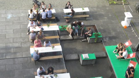 Die Bierbänke, an denen Menschen sitzen, sind mit weißen Tischdecken gedeckt und mit Blumen geschmückt