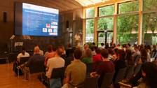 Am Podium steht ein Mann im weißen Hemd vor einer großen Menschen Menge