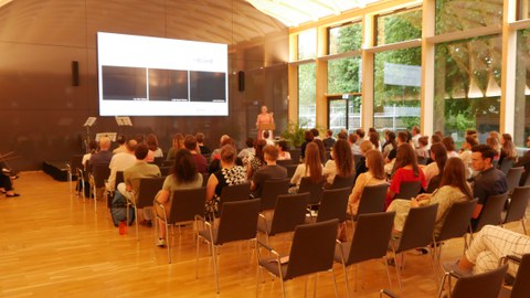 Die letzten Stuhlreihen im Saal sind etwas leerer. Auf der Bühne wird ein Vortrag gehalten