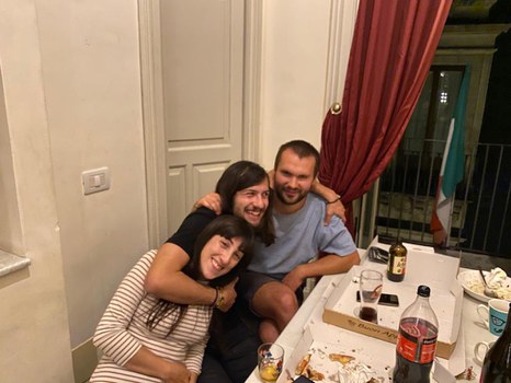 Drei Personen sitzen am Tisch und lachen in die Kamera. 