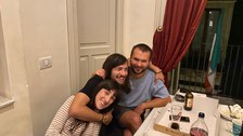 Drei Personen sitzen am Tisch und lachen in die Kamera. 