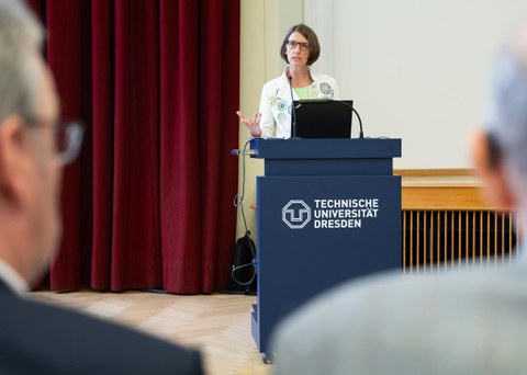 Frau in weißem Blazer steht an einem TU Dresden Pult und spricht zum Publikum