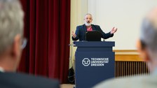Redner mit schwatzem Anzug und rotem Hemd steht am Pult
