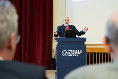 Redner mit schwatzem Anzug und rotem Hemd steht am Pult