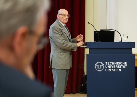 Älterer REdner steht neben dem Pult und doziert
