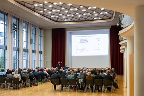 Publikum schaut eine eine Päsentation auf der Leinwamd an