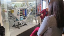 Eine junge Frau steht vor dem Modell des Antimateriedetektors, der an der Raumstation ISS angebracht ist.