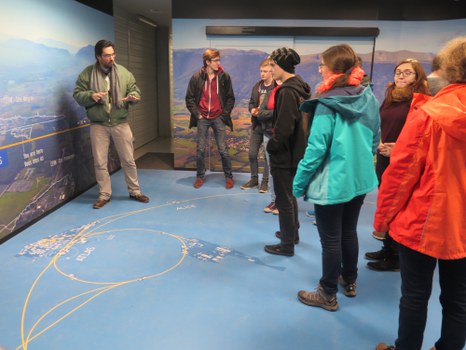 Ein Guide bedeutet den Studierenden auf dem Boden Linien zu begutachten, die auf einer Landkarte die unterirdische Bahn des LHC markieren.