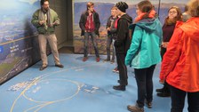 Ein Guide bedeutet den Studierenden auf dem Boden Linien zu begutachten, die auf einer Landkarte die unterirdische Bahn des LHC markieren.