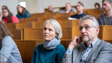 Zwei Menschen sitzen im Hörsaal und schauen nach vorn.