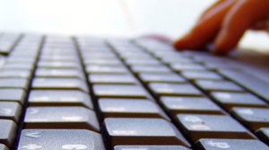 Das Foto zeigt eine Nahaufnahme einer Laptoptastatur, sowie die Hand einer Person, welche den Laptop bedient.